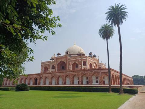Humayun’s Tomb with red sandstone arches and white dome surrounded by manicured lawns and palm trees.