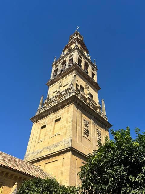 Stone bell tower of the Mosque-Cathedral of Córdoba rising against a clear blue sky.