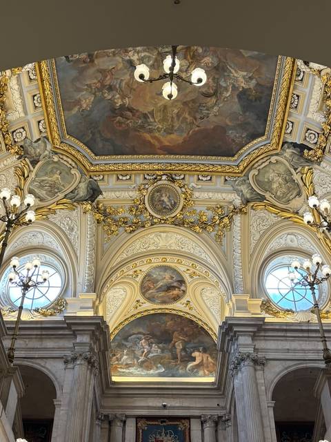 Opulent gilded hall ceiling with baroque paintings and ornate chandeliers.