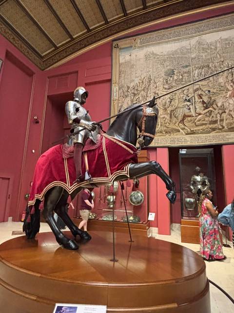 Mounted knight armor exhibit in a museum with red walls and tapestries.