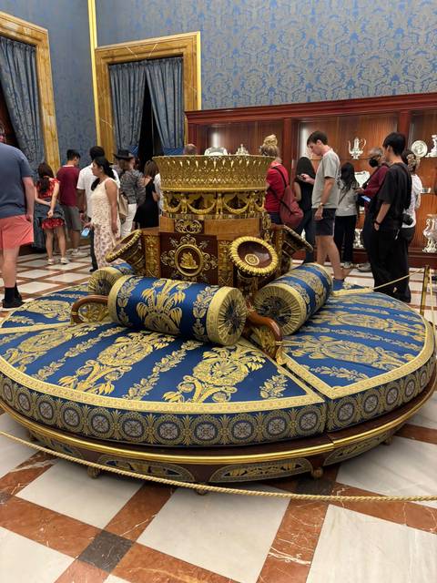 Elaborate blue-and-gold furniture piece surrounded by tourists inside a palace.