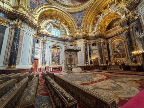 Ornate palace chapel with marble columns, frescoes, and decorative pews.
