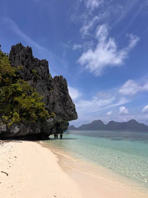 Dramatic limestone cliff jutting over clear sea with distant karst islands.
