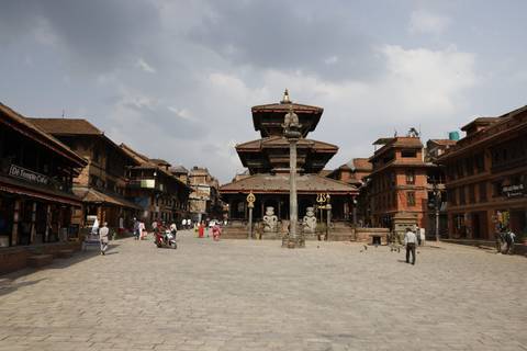 Historic square lined with traditional brick temples and statues under dramatic cloudy sky