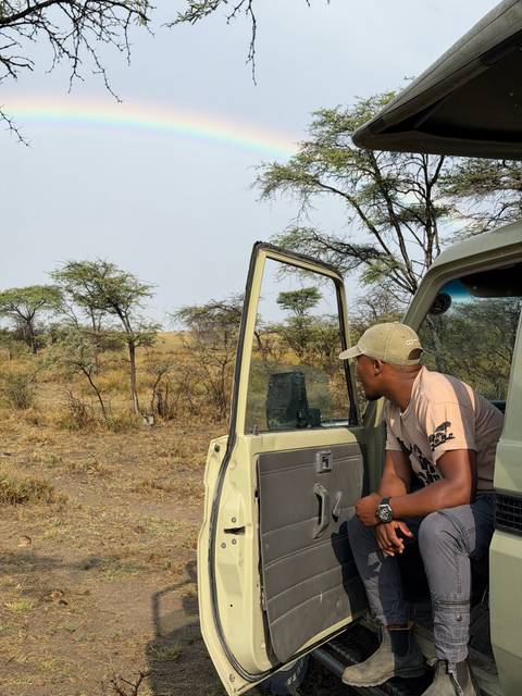 Traveler leaning from an open safari vehicle looking out over dry savanna with scattered acacias.
