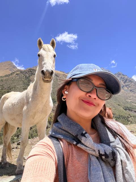 Playful selfie with a white horse and dramatic Andean peaks under a bright blue sky.