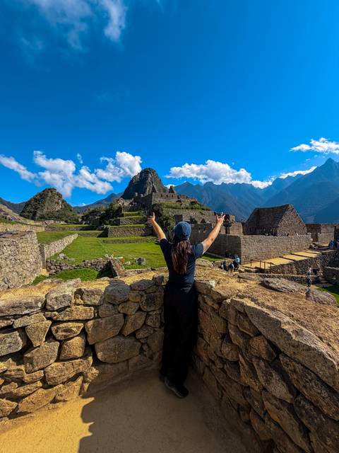 Traveler raises arms in triumph overlooking the stone terraces and peaks of Machu Picchu.