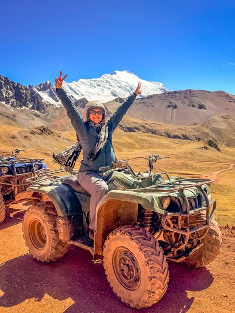 Traveler celebrating atop an ATV with snowy Andes ridges in the background.