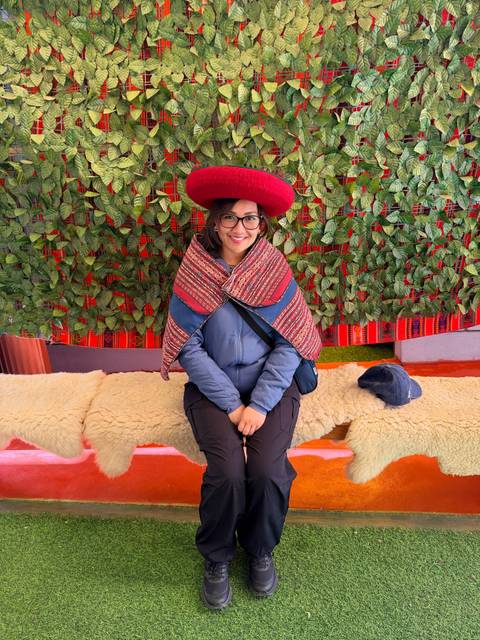 Visitor dressed in traditional Peruvian clothing sitting indoors against a colorful textile backdrop.