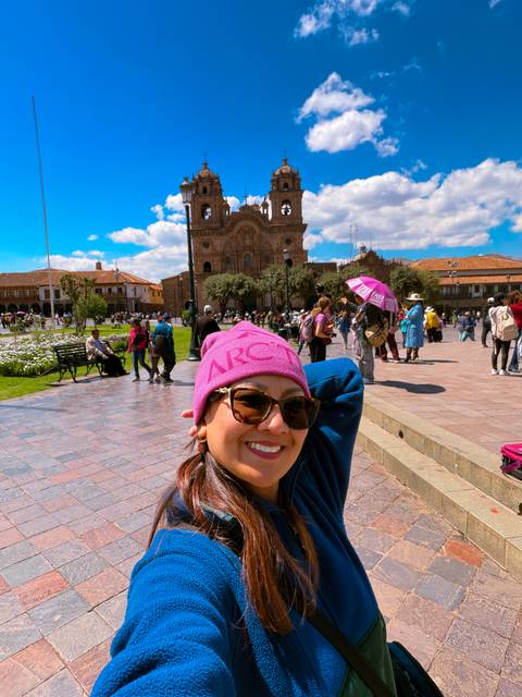 Traveler smiling in Cusco’s Plaza de Armas with the historic cathedral and lively crowd behind.