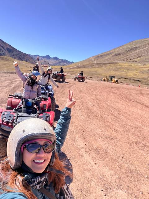 Friends riding red and blue quad bikes on a dusty Andean plateau, throwing peace signs.