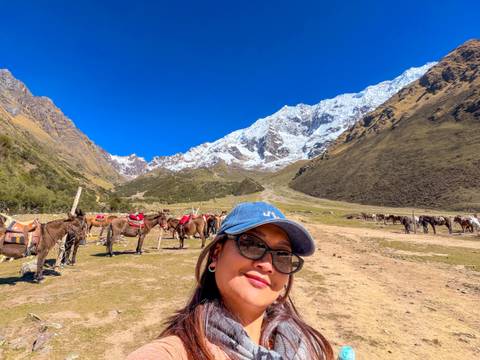 Selfie in a wide valley filled with pack horses below snow-capped peaks and deep blue sky.