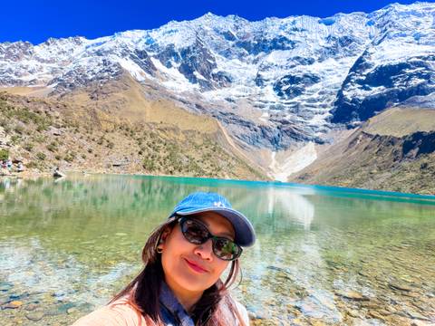 Turquoise Humantay Lake mirrored below sheer snow-covered cliffs with traveler in foreground.