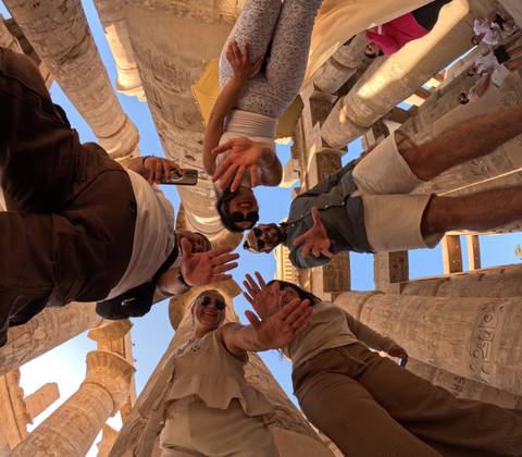Creative low-angle shot of friends reaching toward the camera amid massive hieroglyphic columns.