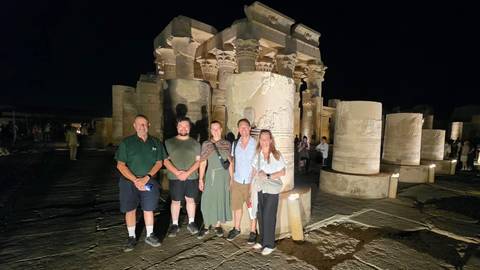 Small tour group posing at night in front of the illuminated columns of Kom Ombo Temple.