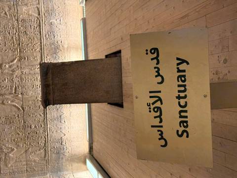 Exhibit plaque reading 'Sanctuary' in Arabic and English with carved relief wall behind.