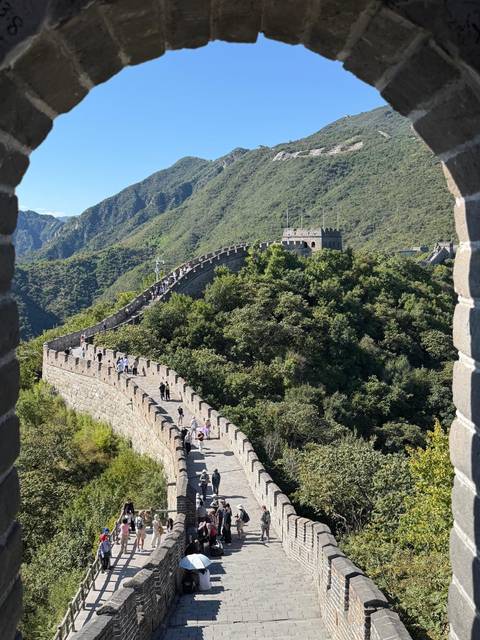 Section of the Great Wall of China winding over forested hills with many visitors walking along the ramparts.