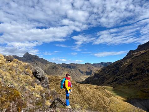 Hiker in colorful gear looks over a vast rugged valley beneath scattered clouds.
