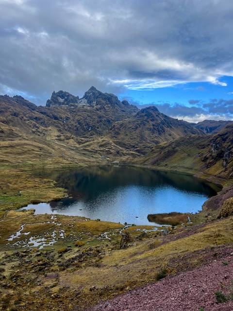 High-altitude lake surrounded by steep brown slopes and jagged peaks under clear skies.