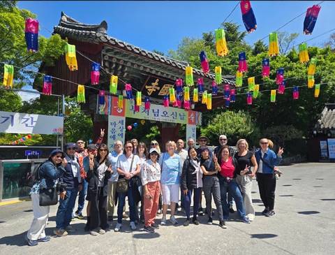 Tour group poses beneath a traditional Korean temple gate decorated with colorful hanging lanterns.