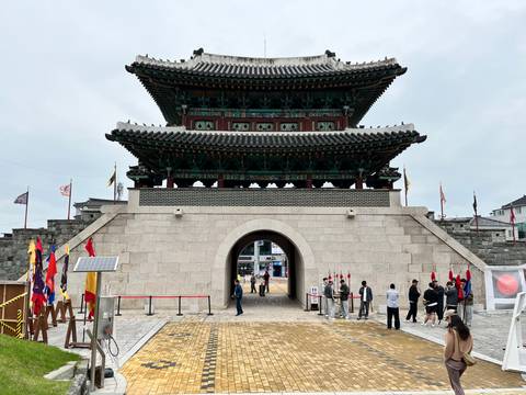 Grand stone fortress gate with multilevel pagoda-style roof and flags, visitors milling around the entrance.