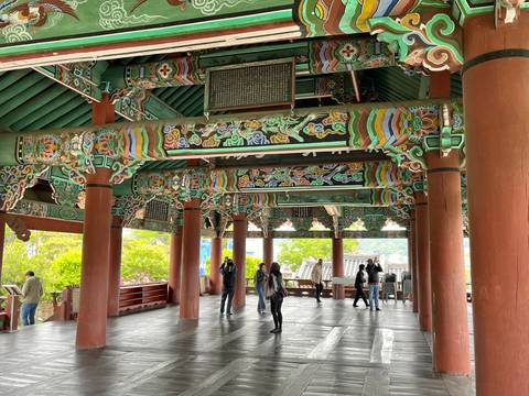 Interior of a Korean pavilion richly painted with colourful patterns and wooden columns, with tourists looking around.
