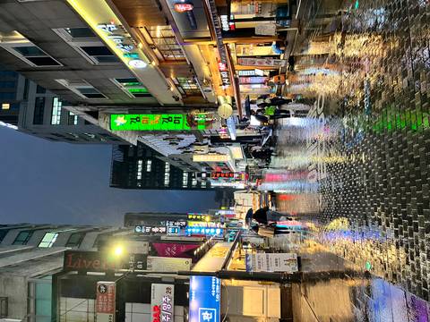 Rain-soaked neon shopping street at night with reflections glistening on cobblestones and people under umbrellas.