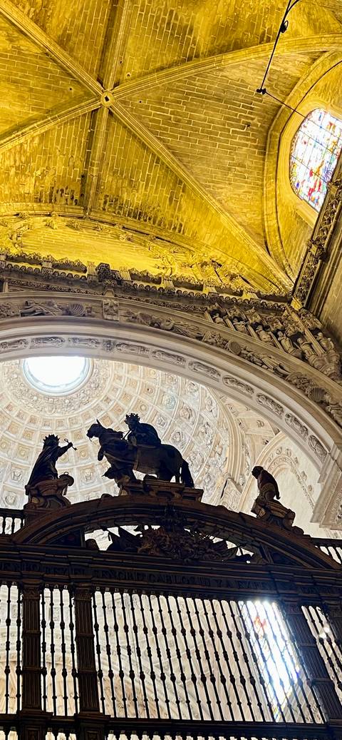 Elaborate carved stone arch and domed ceiling with silhouetted statue figures inside a Spanish cathedral.