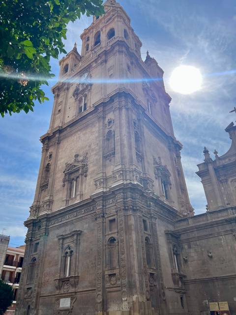 Ornate stone cathedral tower rises into a partly cloudy sky, seen from ground level.