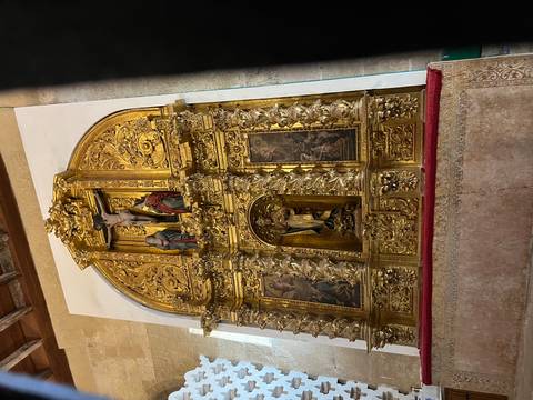 Richly gilded altarpiece with religious sculptures and paintings inside a church sanctuary.
