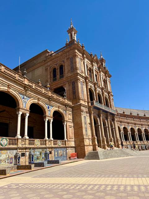 Tower and arched galleries of Plaza de España in warm sunlight against a clear blue sky.