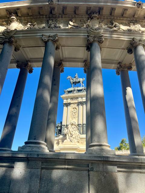 Equestrian monument framed by granite columns under a vivid blue sky in Madrid's Retiro Park.