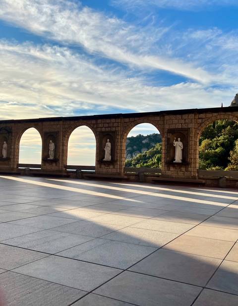 Stone arcade with statues overlooking mountains and sky at Montserrat monastery.