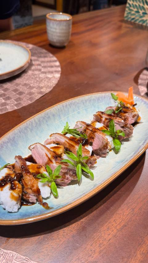 Plated slices of glazed duck breast garnished with herbs arranged neatly on a ceramic dish in a restaurant.