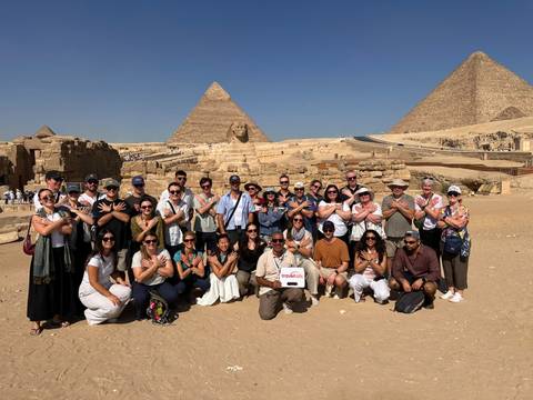 Large tour group posing with crossed-arm gesture in front of the Great Pyramids and Sphinx at Giza.