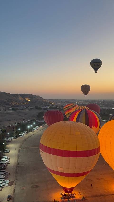 Colourful hot-air balloons rise over the Nile valley at dawn with desert hills in the background.