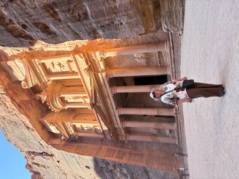 Traveler standing before the ornate Treasury facade carved into rose-red cliffs at Petra.