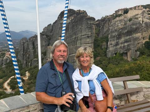 Couple smiling with dramatic Meteora rock pillars rising behind them.