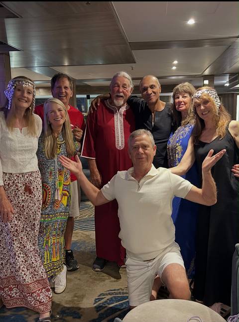 Tour group poses together indoors, some wearing traditional attire, with one man kneeling playfully in front.