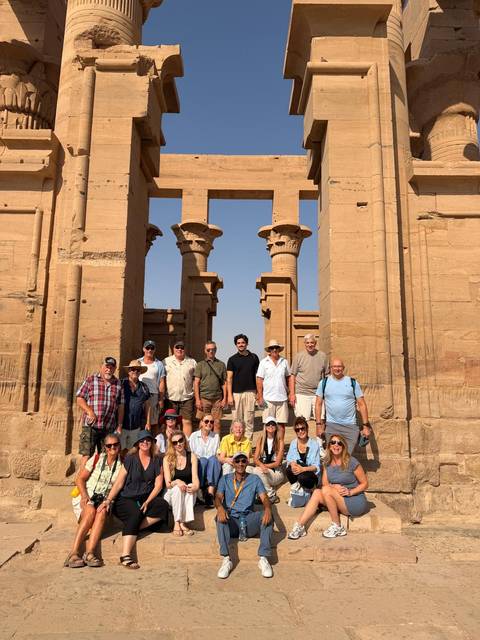 Large tour group stands in front of ancient sandstone columns at an Egyptian temple site.
