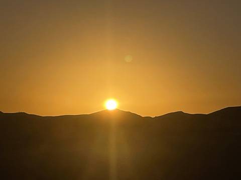 Golden sun setting behind low desert hills casting warm glow across the sky.