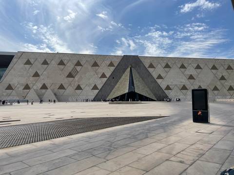 Modern triangular entrance of the Grand Egyptian Museum with expansive geometric façade under wispy clouds.