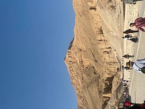 Barren pyramid-shaped mountain rises above the dusty Valley of the Kings with visitors on the path below.