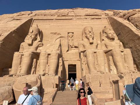 Colossal statues of Ramses II guard the entrance to Abu Simbel temple as early visitors gather below.