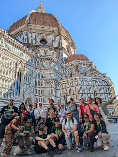 Group standing at the base of Florence’s intricate marble Duomo façade, smiling and wearing green lanyards.