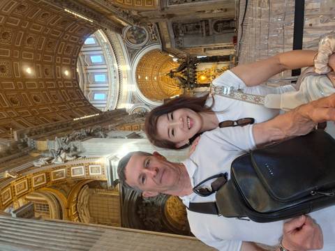Couple inside the ornate interior of St. Peter’s Basilica with soaring dome and gilded decor.