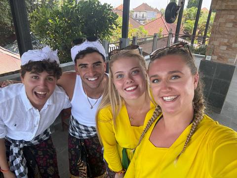 Four friends dressed in yellow and traditional sarongs smiling for a selfie on a terrace.