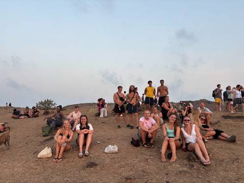 Tourists resting on rocky hillside viewpoint at dusk with scattered groups in background.