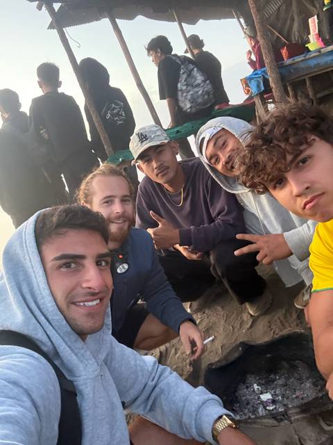 Close-up dawn selfie of friends in hoodies crouching together on mountain summit.