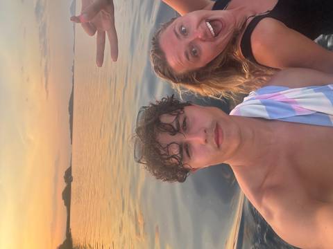 Selfie of two travelers on a boat at calm sea during colorful sunset with distant islets
